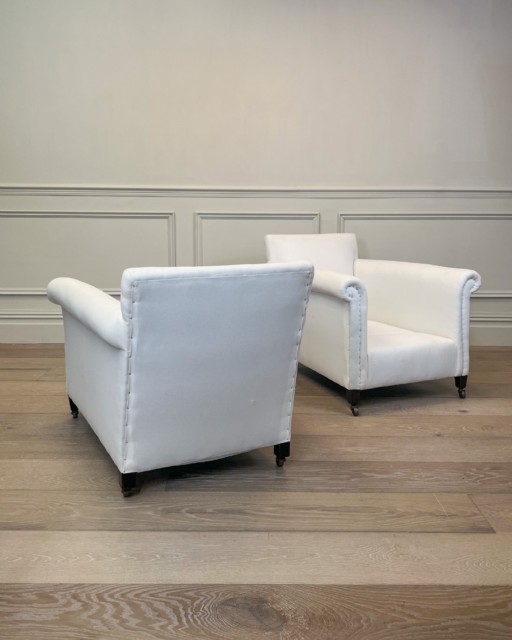 A pair of late nineteenth-century armchairs upholstered in white fabric featuring scroll arms, detail studding, and dark wooden legs with brass castors. View IV