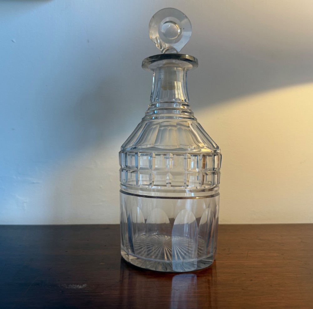 A Georgian clear cut glass decanter featuring a circular disc stopper, geometric panel cuts along the shoulder, and a starburst cut base.