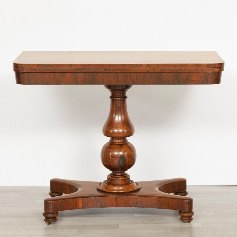 A Regency rosewood card table featuring a fold-over top, turned pedestal column, and quadripartite platform base on turned feet.