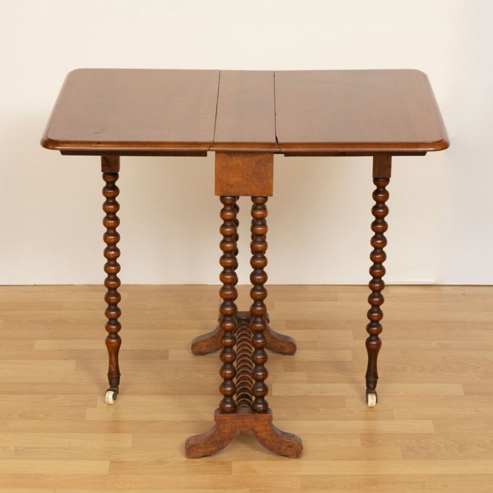 A Victorian walnut drop-leaf side table featuring distinct bobbin-turned legs, a stretcher base, and ceramic castors.