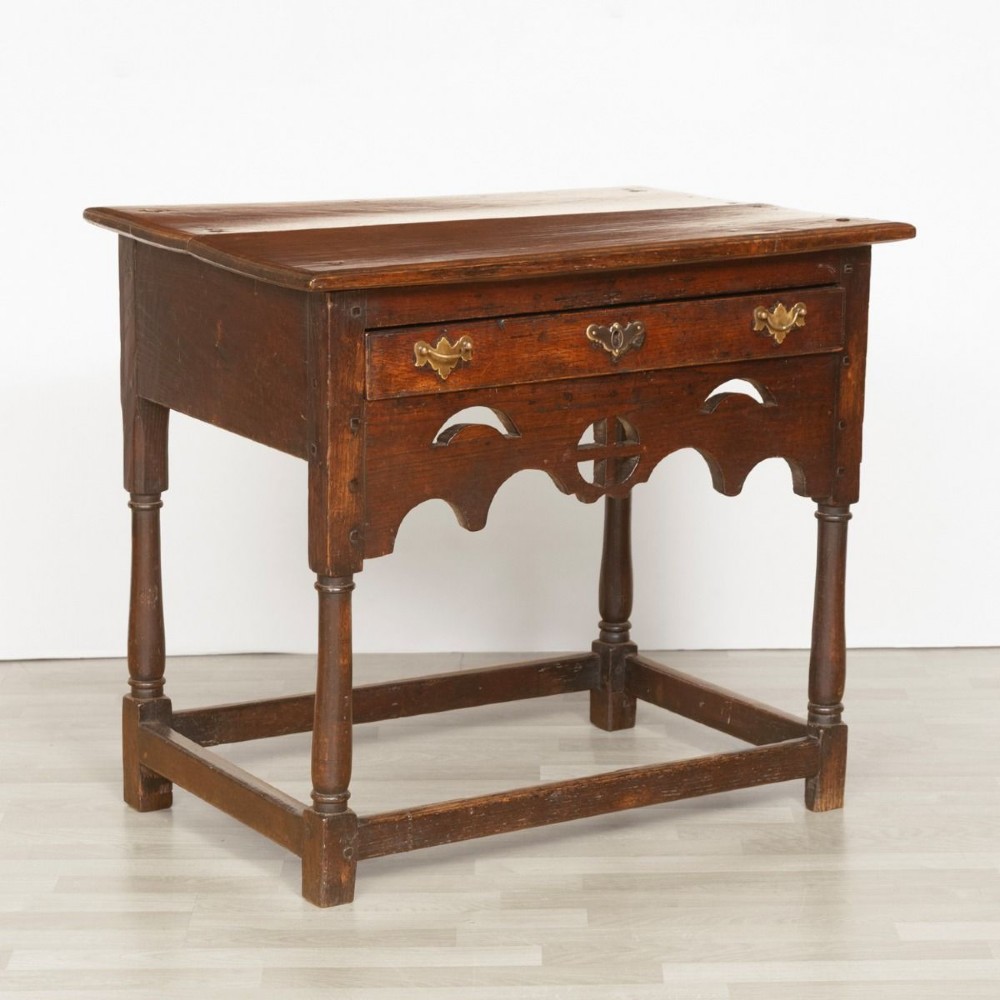 A Georgian dark oak side table featuring a single drawer with brass handles, a decorative pierced apron, turned legs, and a perimeter box stretcher.