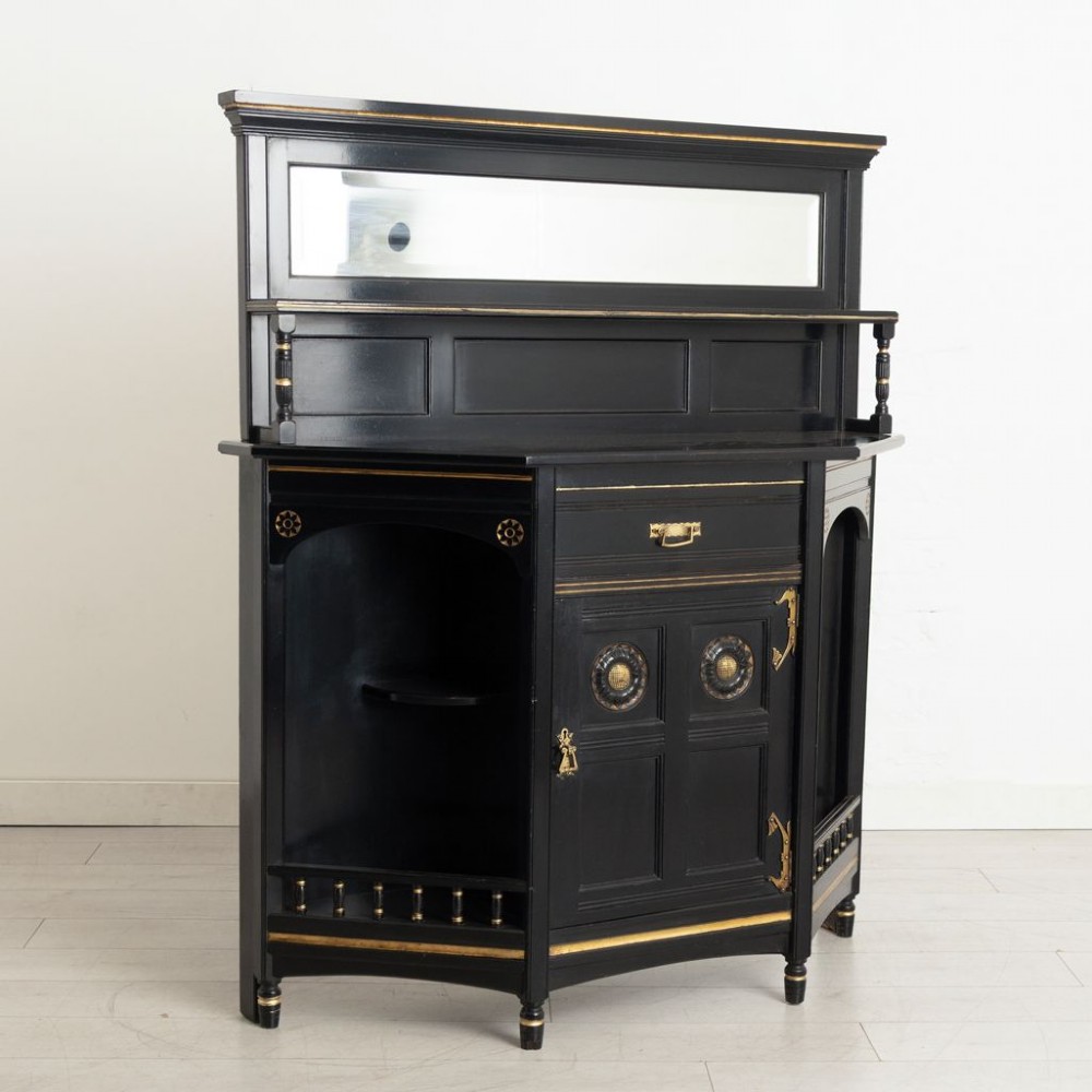 An ebonised black wood cabinet featuring gilded highlights, a mirrored top tier, open side alcoves with turned spindles, and a central cupboard door with carved circular motifs. View II