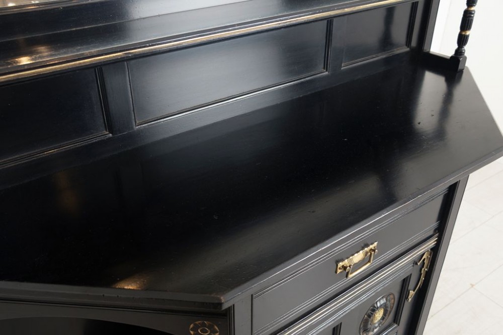 An ebonised black wood cabinet featuring gilded highlights, a mirrored top tier, open side alcoves with turned spindles, and a central cupboard door with carved circular motifs. View III