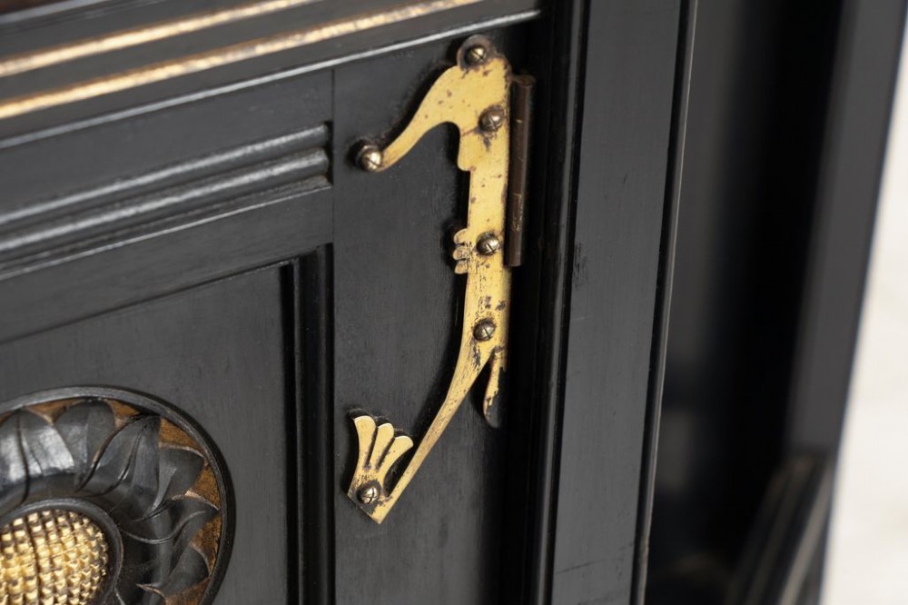 An ebonised black wood cabinet featuring gilded highlights, a mirrored top tier, open side alcoves with turned spindles, and a central cupboard door with carved circular motifs. View V