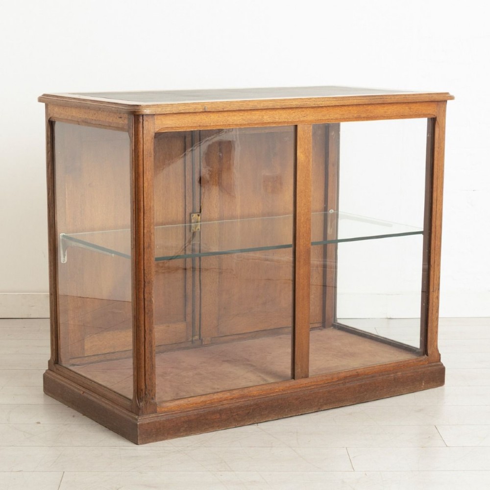 A late 19th-century French oak display case featuring clear glass front and side panels, a single interior glass shelf, and solid timber rear doors.