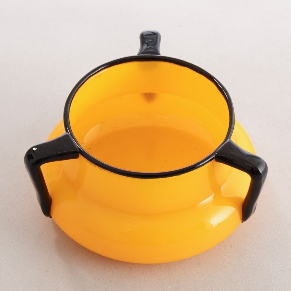 An orange art glass vessel with a squat rounded body, dark black rim, and three black glass handles attached around the top edge. View II