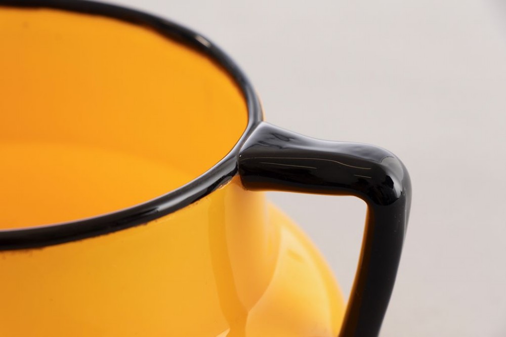 An orange art glass vessel with a squat rounded body, dark black rim, and three black glass handles attached around the top edge. View III