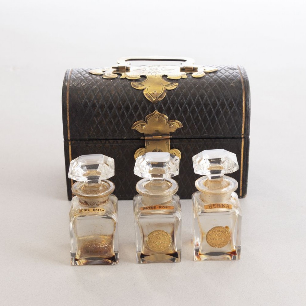 An open black leather box lined with purple velvet containing three clear glass perfume bottles with octagonal faceted stoppers. View II