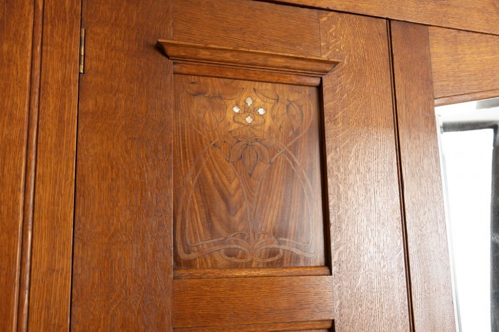 A large oak three-door Arts and Crafts wardrobe featuring a central arched mirror flanked by stylized inlaid panels over two lower drawers. View VI