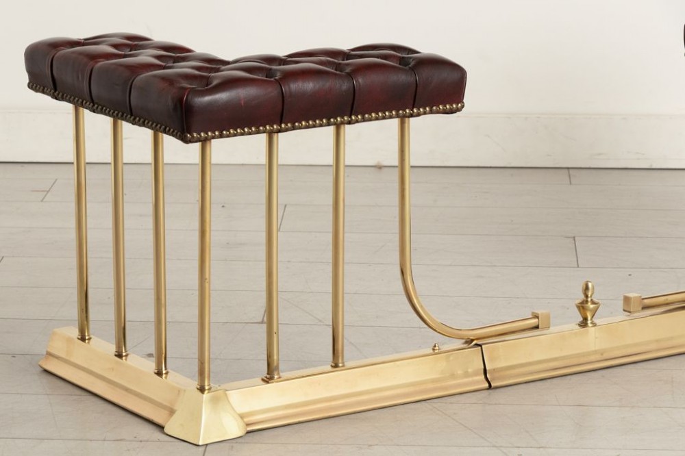 An Edwardian polished brass club fender featuring twin burgundy leather buttoned seats supported by vertical brass rails on a shaped base. View III