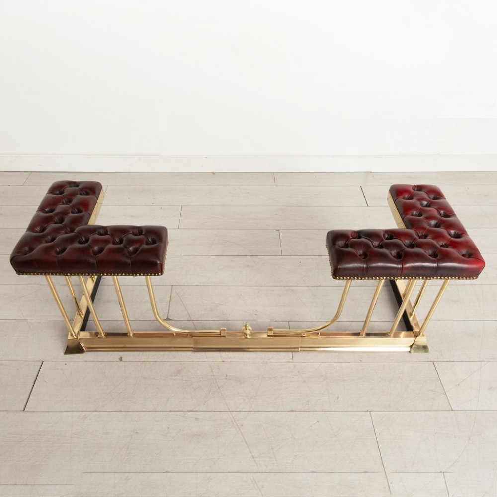 An Edwardian polished brass club fender featuring twin burgundy leather buttoned seats supported by vertical brass rails on a shaped base. View IV