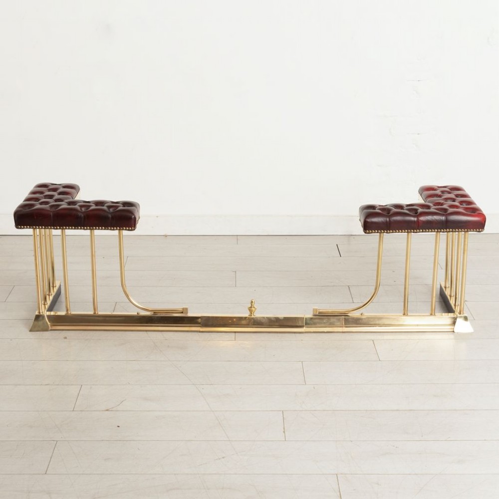 An Edwardian polished brass club fender featuring twin burgundy leather buttoned seats supported by vertical brass rails on a shaped base. View V