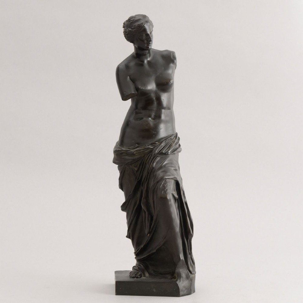 A dark brown bronze sculpture depicting the Venus de Milo draped in cloth around the lower body, mounted on an integrated rectangular base.