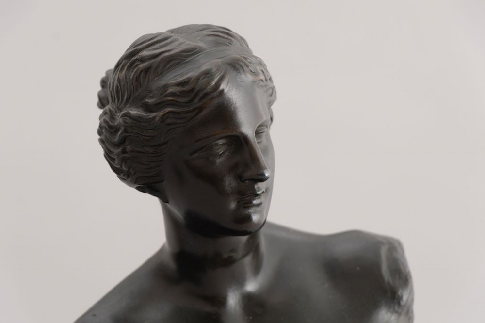 A dark brown bronze sculpture depicting the Venus de Milo draped in cloth around the lower body, mounted on an integrated rectangular base. View III