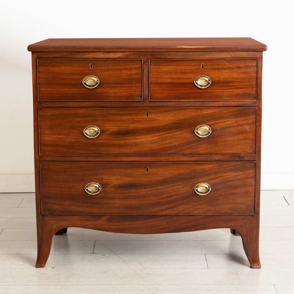 A small Georgian mahogany chest of drawers featuring two short drawers over two long drawers with brass oval handles and splayed feet.