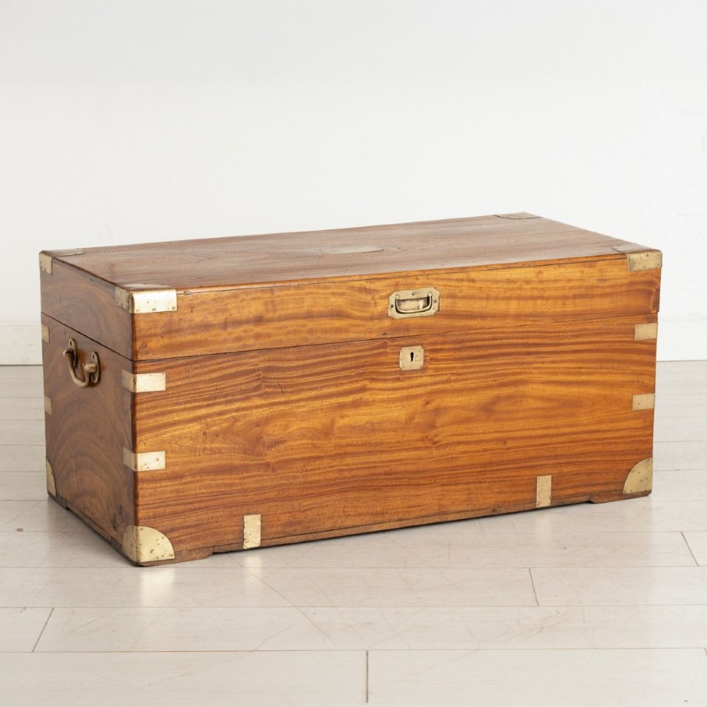 A warm brown rectangular camphor wood campaign chest featuring flush brass corner brackets, recessed carrying handles, and a flat hinged lid.