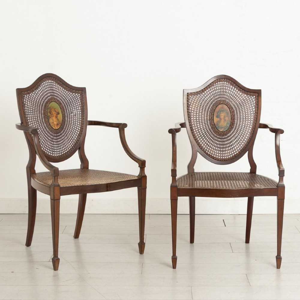 A pair of dark wood Louis XVI style armchairs featuring woven cane seats and backs centred with oval painted portrait medallions.