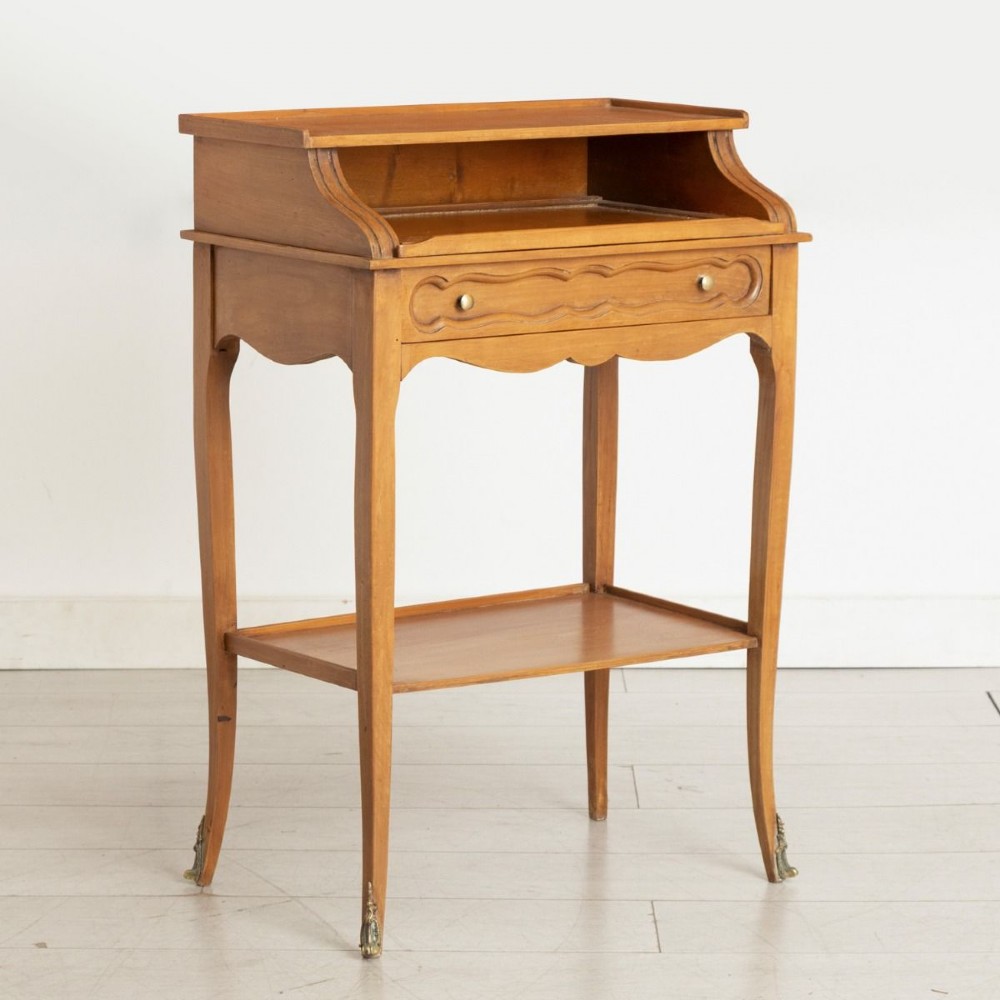 A small French provincial style fruitwood writing table with an upper gallery shelf, single drawer, lower tier shelf, cabriole legs, and brass sabot feet.