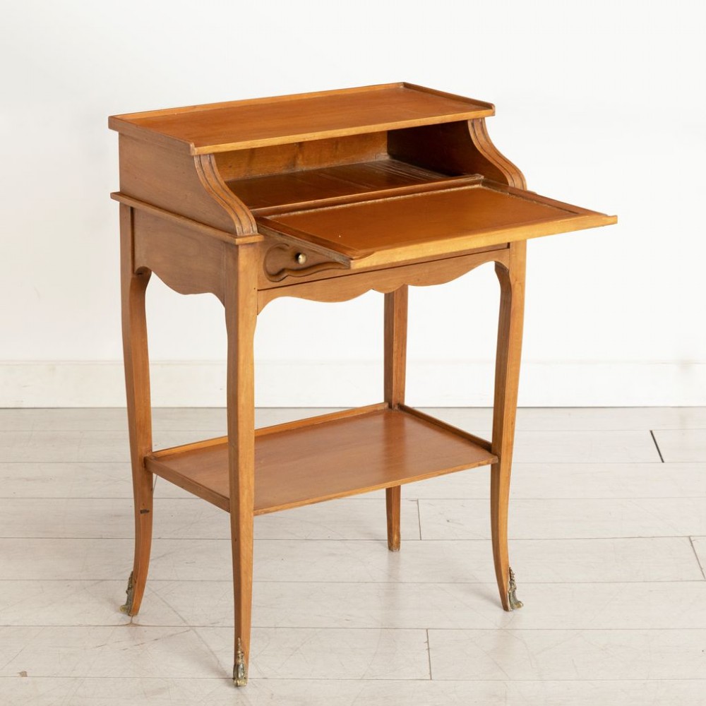 A small French provincial style fruitwood writing table with an upper gallery shelf, single drawer, lower tier shelf, cabriole legs, and brass sabot feet. View III