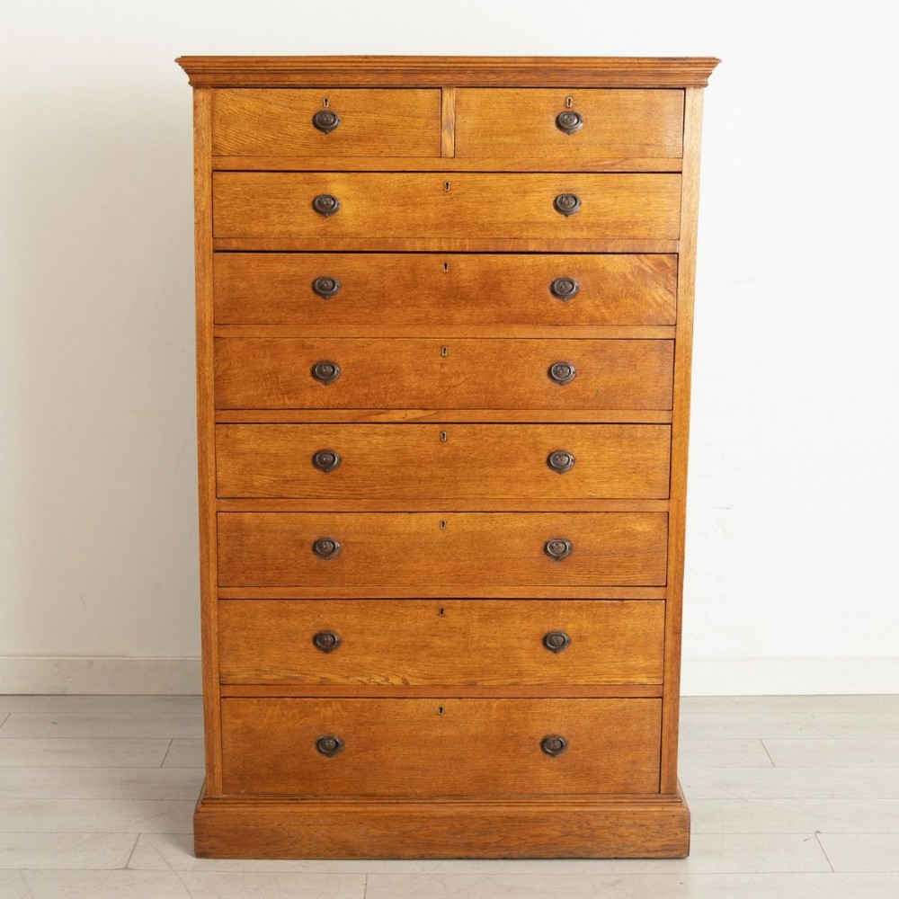 A tall Arts and Crafts period oak chest featuring two short drawers above seven long graduated drawers with dark metal ring pull handles.