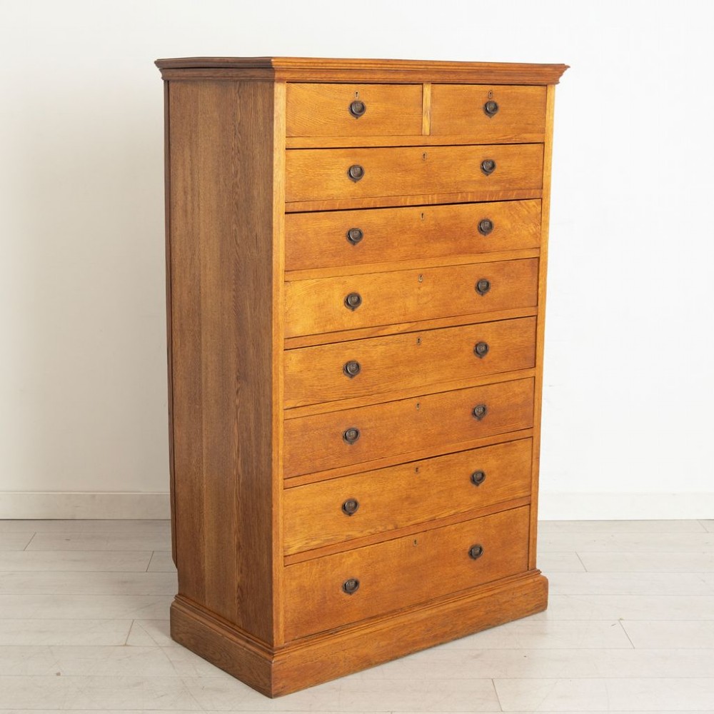 A tall Arts and Crafts period oak chest featuring two short drawers above seven long graduated drawers with dark metal ring pull handles. View II