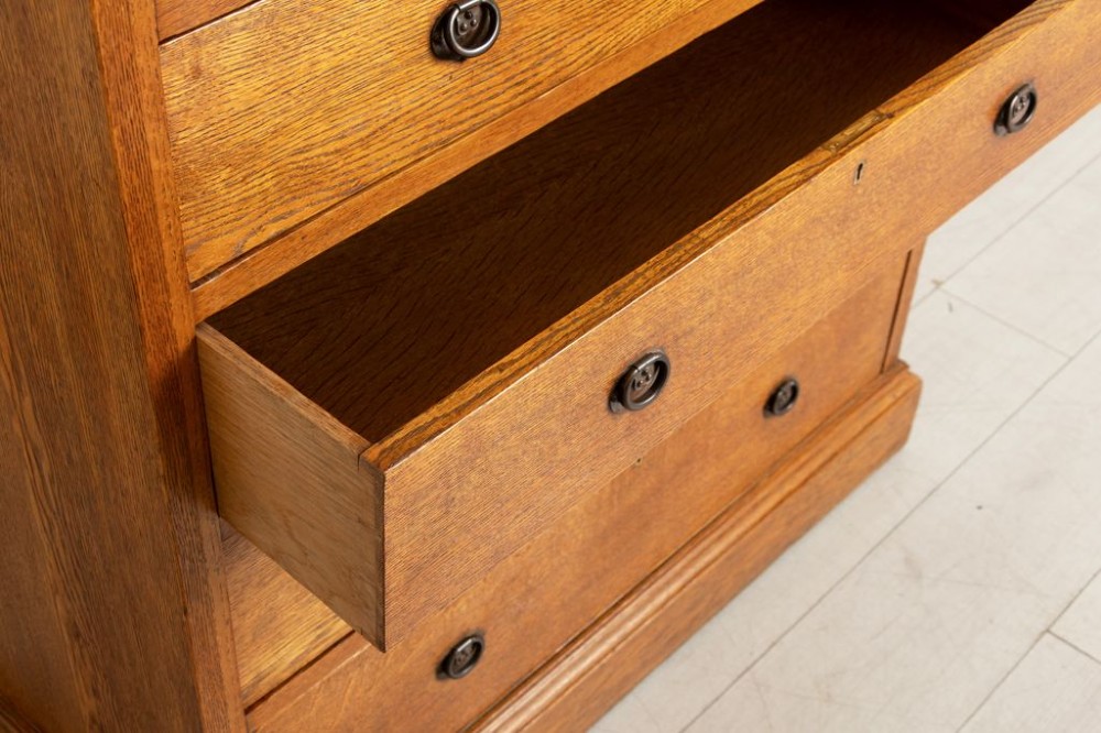 A tall Arts and Crafts period oak chest featuring two short drawers above seven long graduated drawers with dark metal ring pull handles. View III