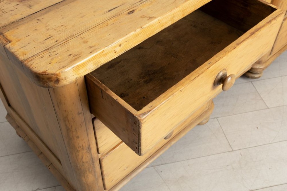 A 19th-century honey pine dresser base featuring six side drawers flanking a central arched cupboard door resting on turned bun feet. View III