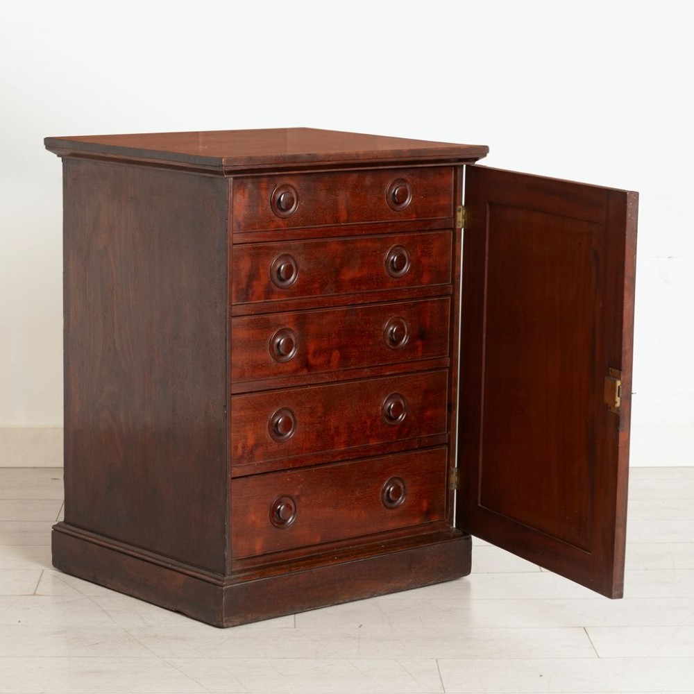 A dark mahogany musicians cabinet with an open single panel door revealing five shallow drawers with turned circular knobs.