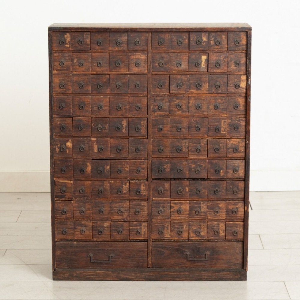 A tall dark timber Japanese apothecary cabinet featuring multiple small rectangular drawers with iron ring pulls above two wider base drawers.
