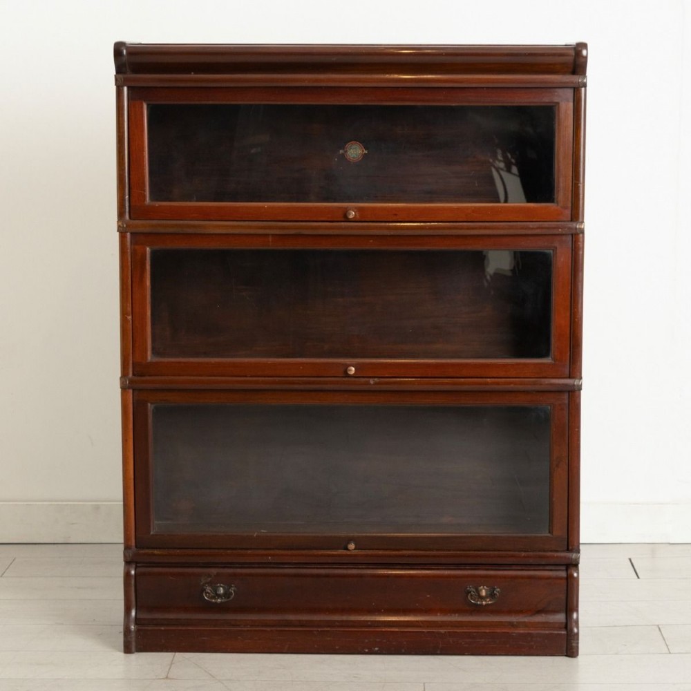 An antique mahogany three-tier Globe Wernicke sectional bookcase featuring glass up-and-over doors and a base drawer.