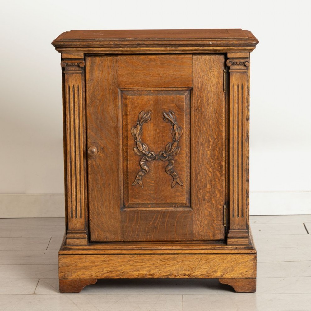 A late nineteenth-century oak side cupboard featuring a single panelled door decorated with a carved laurel wreath motif and flanked by fluted pilasters. View II