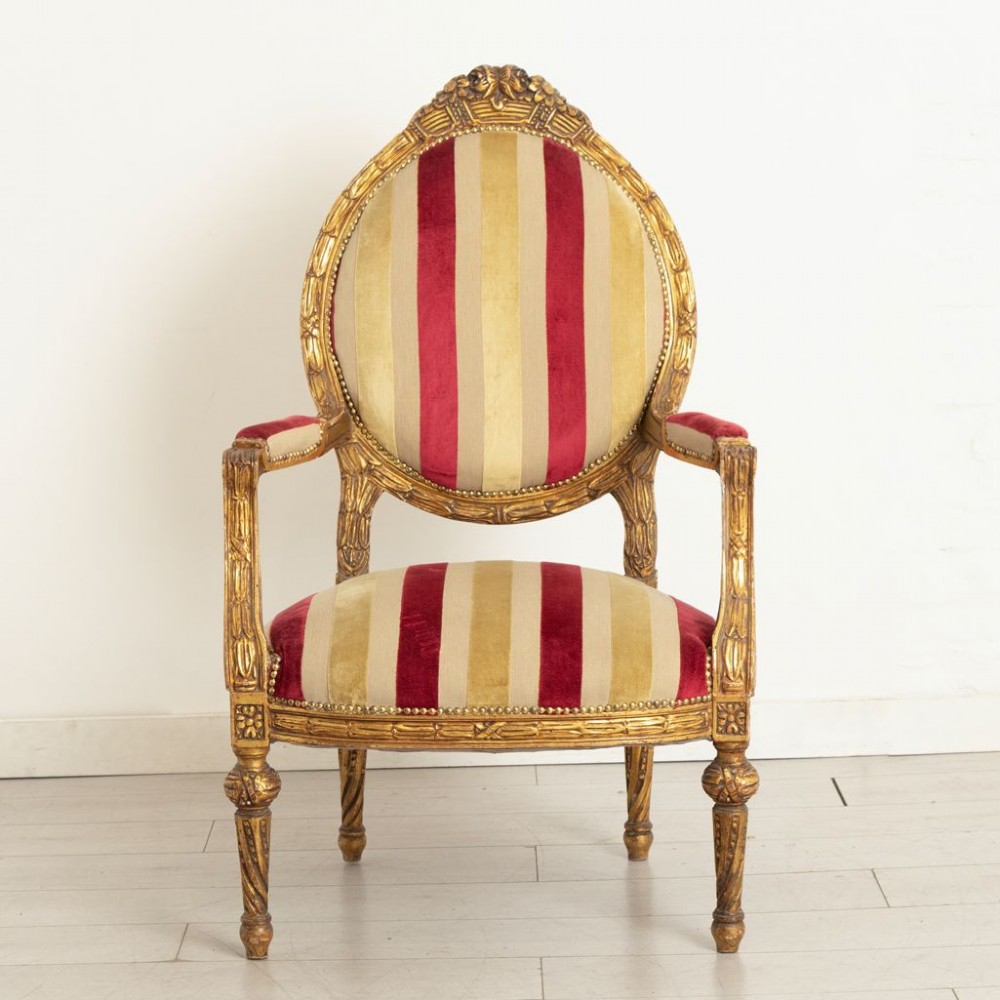 A French Louis XVI style open armchair featuring a carved gold giltwood frame, oval backrest, fluted legs, and red and cream striped velvet upholstery.