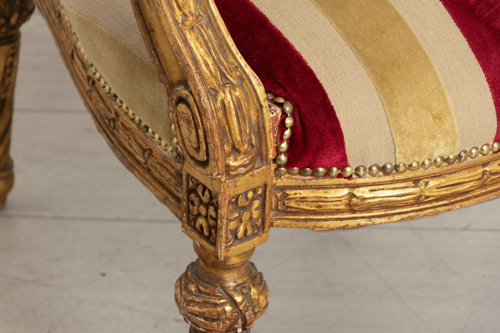 A French Louis XVI style open armchair featuring a carved gold giltwood frame, oval backrest, fluted legs, and red and cream striped velvet upholstery. View III