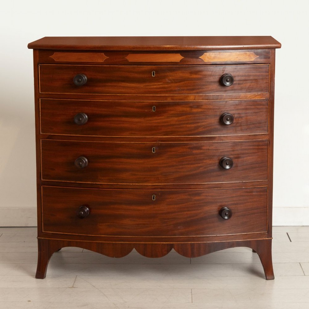A Georgian flame mahogany bowfront chest of drawers featuring four graduated drawers with turned handles, marquetry inlay, and splayed bracket feet.