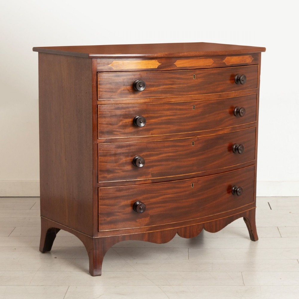 A Georgian flame mahogany bowfront chest of drawers featuring four graduated drawers with turned handles, marquetry inlay, and splayed bracket feet. View II