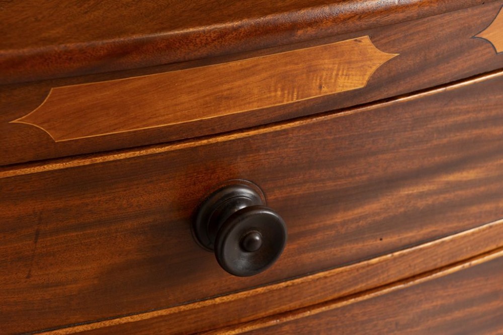A Georgian flame mahogany bowfront chest of drawers featuring four graduated drawers with turned handles, marquetry inlay, and splayed bracket feet. View III
