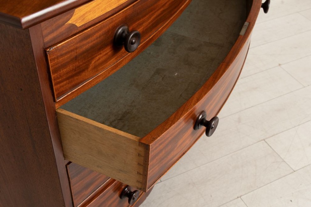 A Georgian flame mahogany bowfront chest of drawers featuring four graduated drawers with turned handles, marquetry inlay, and splayed bracket feet. View IV