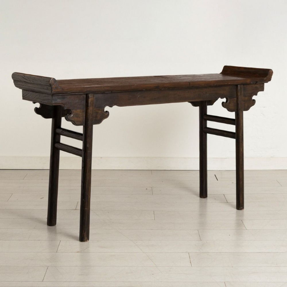 A dark timber Chinese altar table featuring everted end flanges, carved spandrels, round legs, and side stretchers on a plain white background.