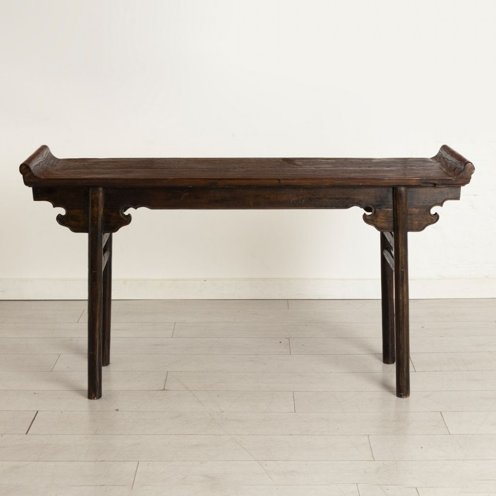 A dark timber Chinese altar table featuring everted end flanges, carved spandrels, round legs, and side stretchers on a plain white background. View II