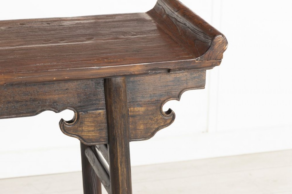 A dark timber Chinese altar table featuring everted end flanges, carved spandrels, round legs, and side stretchers on a plain white background. View III