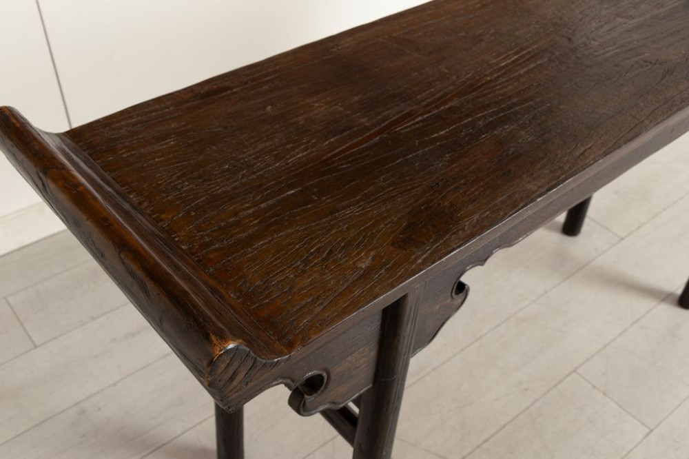 A dark timber Chinese altar table featuring everted end flanges, carved spandrels, round legs, and side stretchers on a plain white background. View IV