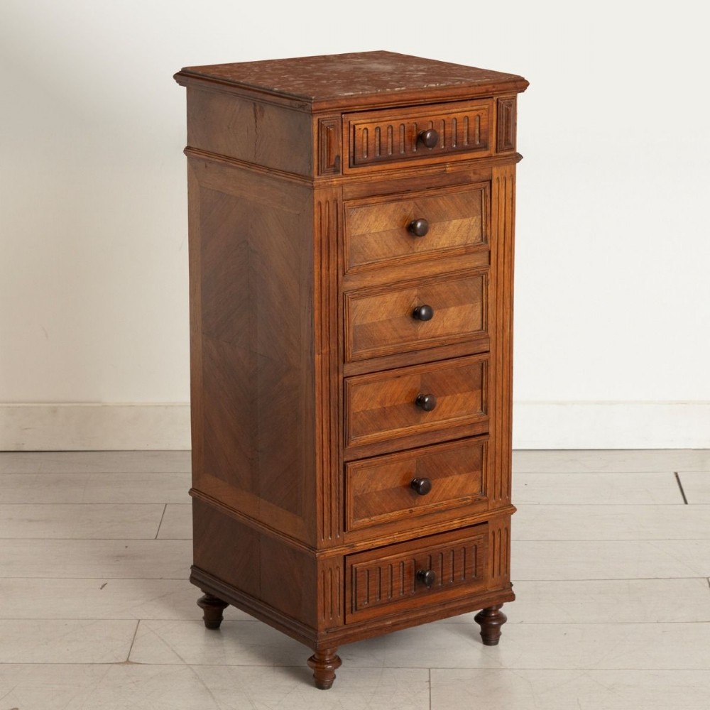 An antique French rosewood bedside chest featuring six drawers, chevron parquetry veneer, fluted side columns, turned feet, and an inset brown marble top.