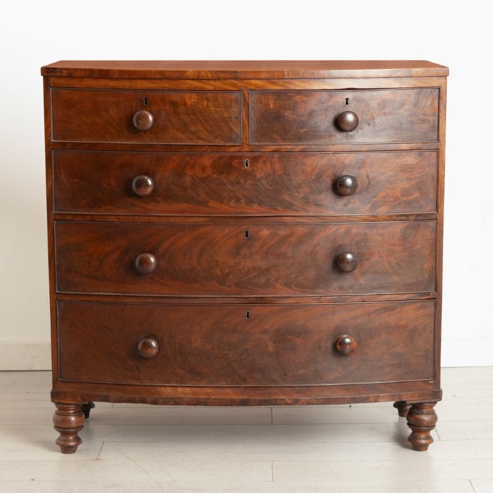A Victorian mahogany bowfront chest of drawers featuring two short upper drawers and three long lower drawers with turned wooden knobs and turned feet.