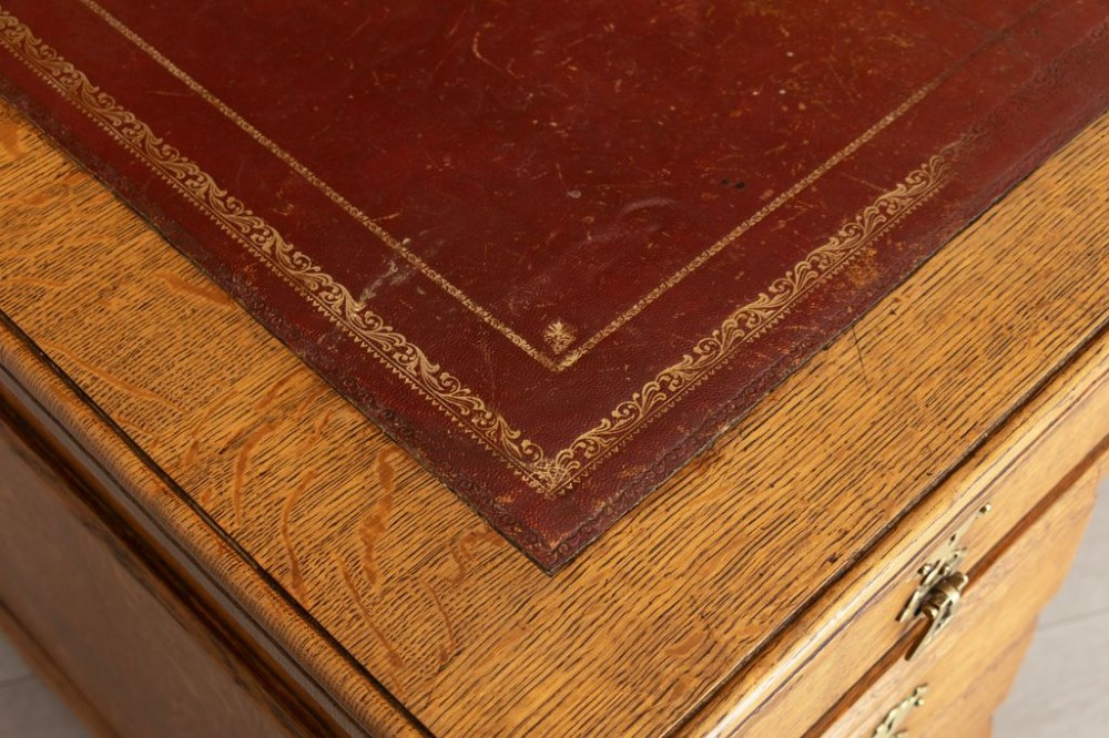 An Arts and Crafts golden oak pedestal desk featuring an inset leather writing surface, twin pedestals with brass handles, and castors. View IV