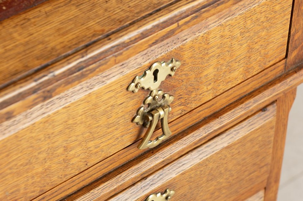 An Arts and Crafts golden oak pedestal desk featuring an inset leather writing surface, twin pedestals with brass handles, and castors. View V