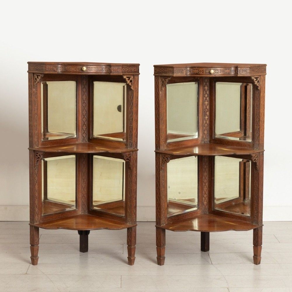 A pair of late 19th-century mahogany corner display cabinets featuring mirrored back panels, carved open shelves, and turned legs.