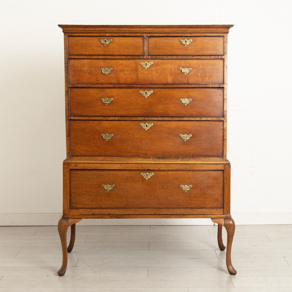 An 18th-century oak chest on stand featuring multiple graduated drawers with brass hardware, raised on four shaped cabriole legs.