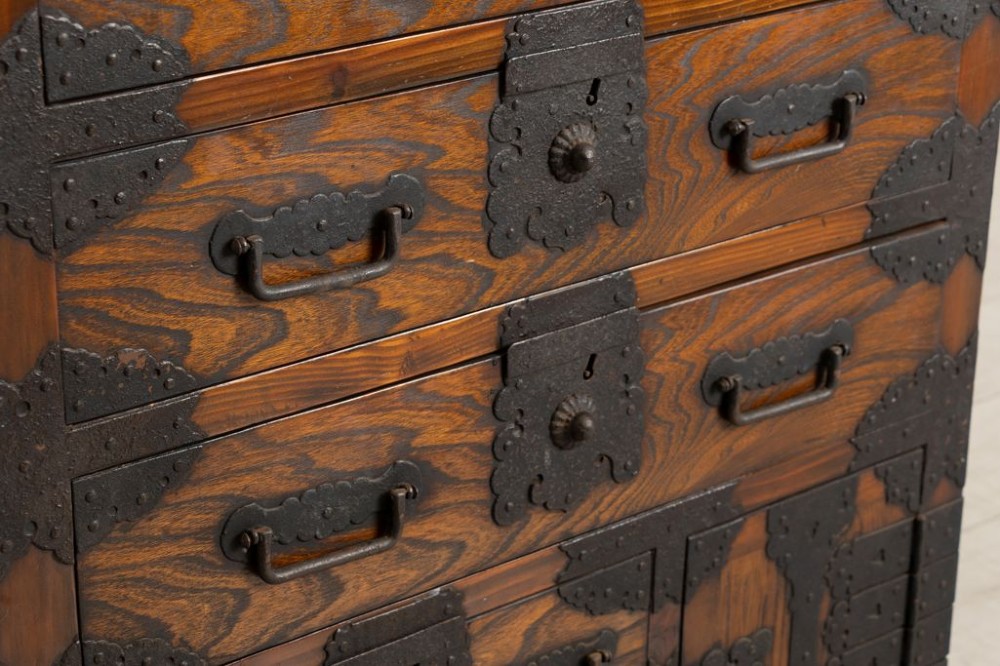 An antique Japanese zelkova wood chest of drawers featuring dark iron corner brackets, lock plates, drop handles, and integrated wooden wheels at the base. View IV