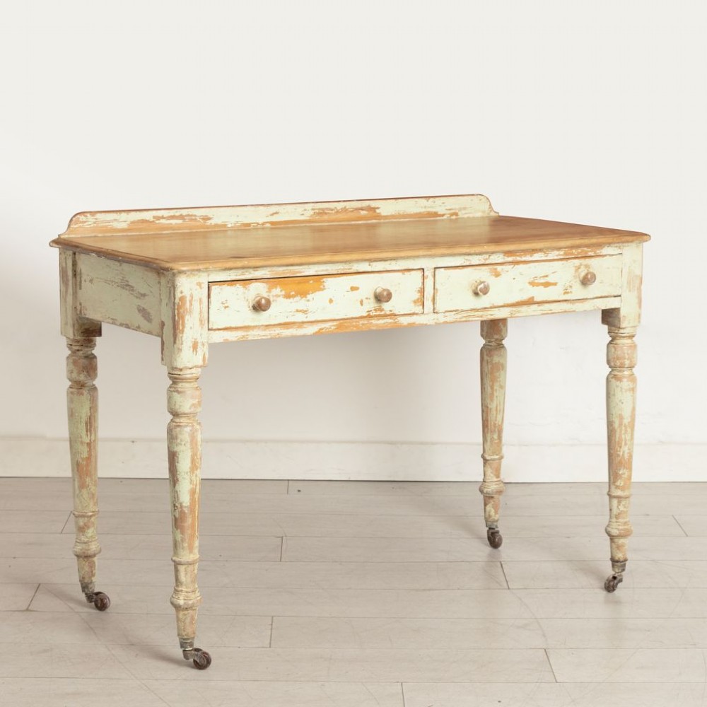 A 19th-century birch writing table with a polished natural timber top, two drawers with wooden knobs, distressed off-white painted turned legs, and brass castors. View II