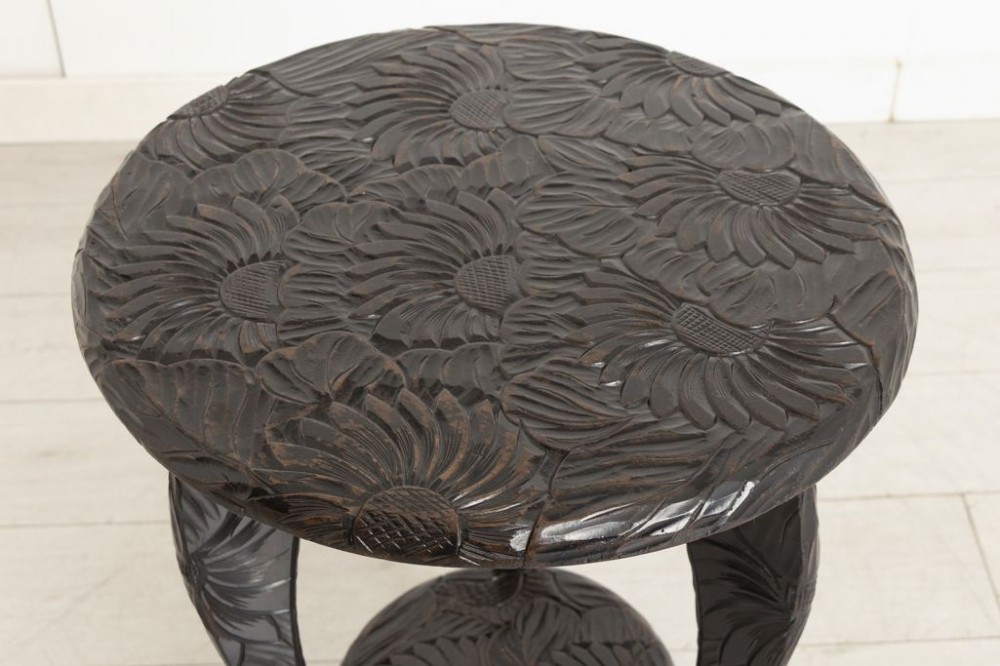 A dark-stained wooden side table featuring a circular top and three outward-curving legs detailed with relief floral carvings and a small lower shelf. View II